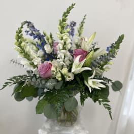 Mixed bouquet of white lilies, pink roses, and blue flowers in a glass vase