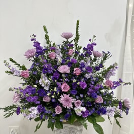 Large purple and pink floral arrangement in a decorative pedestal vase