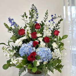 Red roses, blue hydrangeas, and white flowers in a basket arrangement