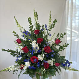 Tall arrangement of red roses, white snapdragons, and blue flowers in a basket