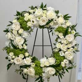 White floral wreath on a black stand with green accents