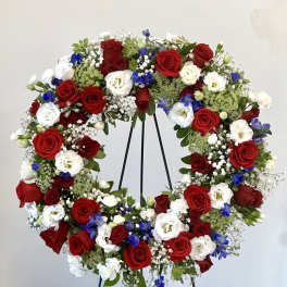 Heart-shaped wreath of red, white, and blue flowers on a black stand