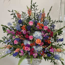 Large mixed floral arrangement with roses, hydrangeas, and snapdragons in a pedestal vase
