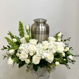 White rose and tulip arrangement in a decorative urn with a silver urn behind it