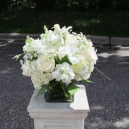 White floral arrangement in a square vase on a pedestal