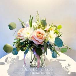 Peach roses and white flowers in a clear glass vase with eucalyptus
