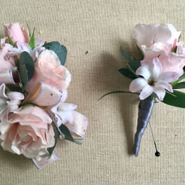 Two pale pink floral boutonnieres with ribbon and greenery on a beige background