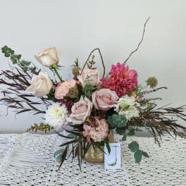 Blush and white floral arrangement in a gold vase with long burgundy foliage