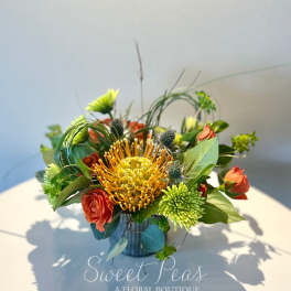 Orange pincushion protea with red roses in a small vase