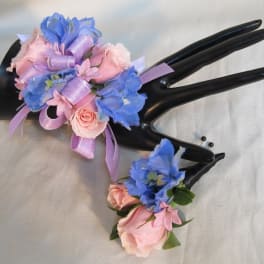 Two floral corsages with pink and blue flowers on black display hands