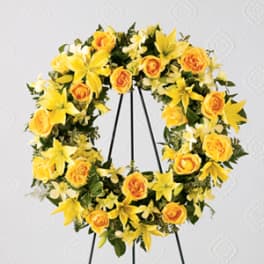Yellow floral wreath with roses and lilies on a black stand