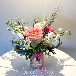Pink gerbera bouquet in a glass vase with white blooms and a ribbon