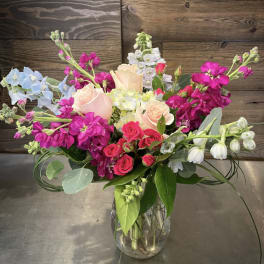 Mixed bouquet of pink, white, and blue flowers in a clear glass vase