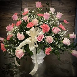 Pink roses and carnations in a white vase with a cream ribbon