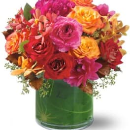 Bright mixed bouquet of roses and orchids in a green glass vase