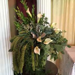 Tall arrangement of cream calla lilies and abundant cascading greenery in a clear glass vase
