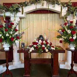 Symmetrical funeral floral display with red and white arrangements on pedestals and a table centerpiece