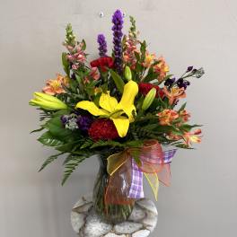 Mixed bouquet with yellow lilies, red carnations, and purple flowers in a glass vase