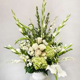 Tall white and green arrangement with roses, hydrangeas and gladiolus in a white pedestal vase