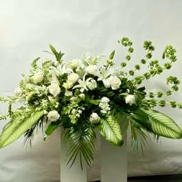 White floral arrangement with roses and lilies in a tall white pedestal vase