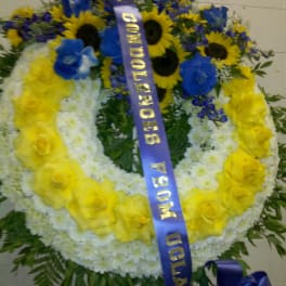 Large floral wreath with yellow roses, white flowers, and blue blooms