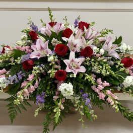 Long floral arrangement with red roses and pink lilies on a wooden table