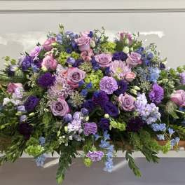 Large purple and pink floral casket spray with trailing greenery