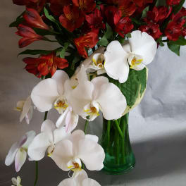 Bouquet of red alstroemeria and white orchids in a green glass vase