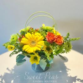 Yellow and orange flower arrangement in a handled container