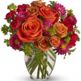Orange roses and magenta daisies in a clear glass vase
