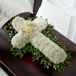White floral casket spray with roses and round blooms on dark wood