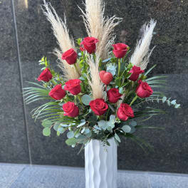Tall arrangement of red roses with pampas grass in a white vase
