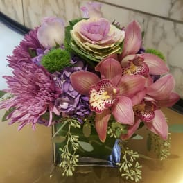 Purple and pink floral arrangement in a square glass vase