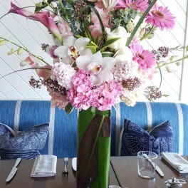 Tall pink and white floral arrangement in a glass vase on a dining table
