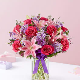 Bouquet of pink roses and lilies in a clear glass vase with a purple ribbon