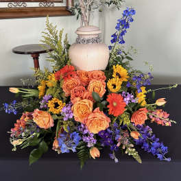Colorful floral arrangement with roses, gerbera daisies, and blue delphinium around an urn