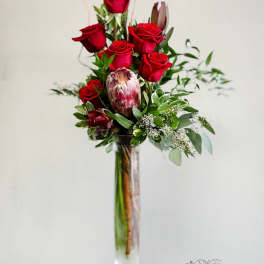 Tall vase arrangement of red roses with greenery and a protea