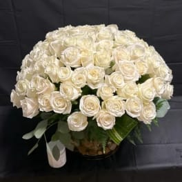 Large dome of cream roses in a clear vase with a white candle on a black background