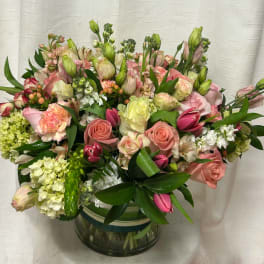 Low glass vase of pink and cream roses, tulips, carnations, and hydrangeas in a lush mixed arrangement