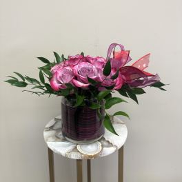 Low arrangement of bright pink roses in a glass cylinder vase with pink ribbon accents.