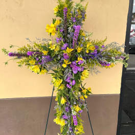 Tall floral cross on an easel with yellow and purple flowers