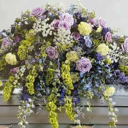 Lavender and blue floral casket spray with trailing greenery