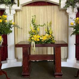 Yellow rose arrangements on pedestals around a wooden table