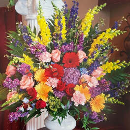 Tall mixed arrangement of bright roses, gerbera daisies, carnations and snapdragons in a white vase.