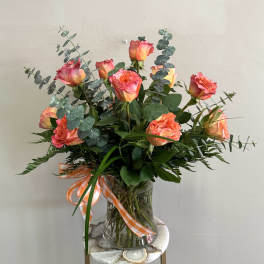 Pink-orange roses in a clear glass vase with eucalyptus and a ribbon
