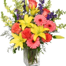 Mixed bouquet of yellow lilies, pink gerbera daisies, and roses in a clear glass vase