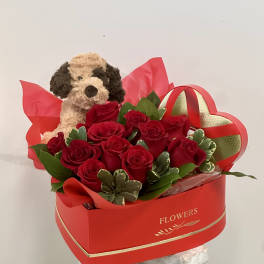 Red roses in a heart-shaped box with a plush dog