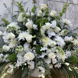 Large white floral arrangement with roses and orchids in a white container