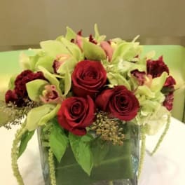 Red roses and pale green orchids in a square glass vase