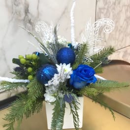 Blue rose arrangement with pine branches and ornaments in a white vase